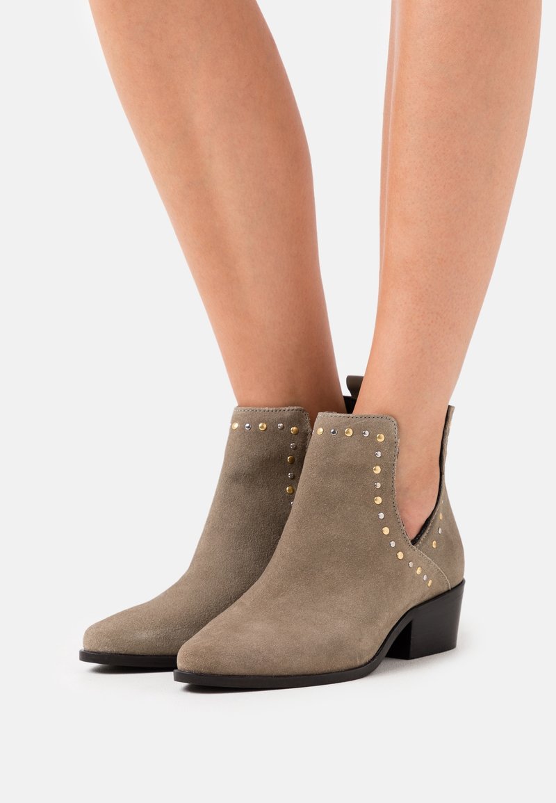 Stivaletti alla caviglia color taupe in suede, con borchie dorate e argentate lungo i lati, punta appuntita e tacco basso a blocco.