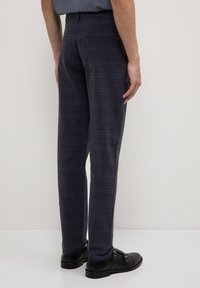 Pantalons à carreaux bleu marine avec une coupe droite, dotés d'une poche à l'arrière et portés avec des chaussures noires. Le tissu a une texture lisse.