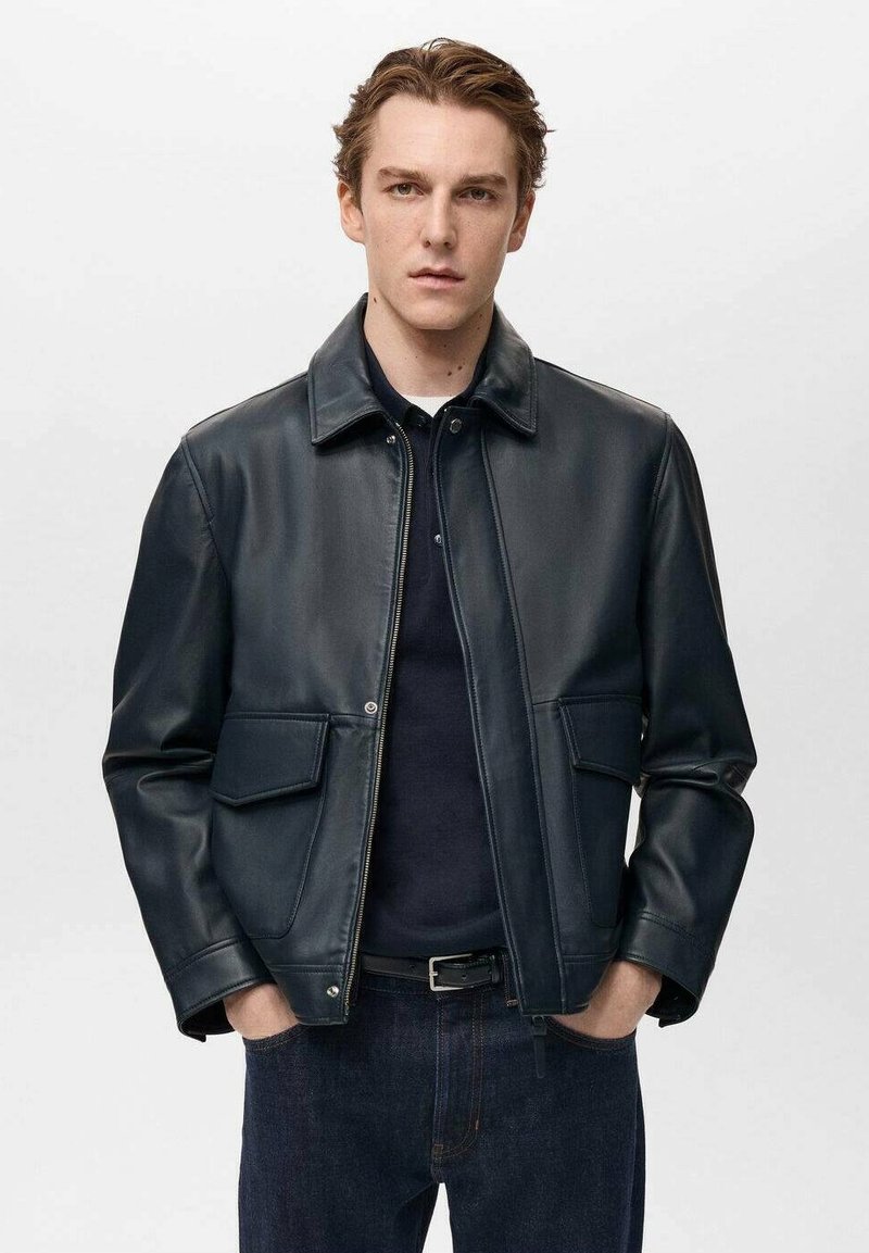 Dunkelblaue Lederjacke mit Reißverschluss, Punktkragen, zwei vorderen Taschen und glatter Textur, kombiniert mit einem schwarzen Hemd und dunklen Jeans.
