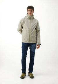 Light gray waterproof jacket with a high collar, front zipper, and black cuffs, paired with dark blue pants and green hiking shoes.