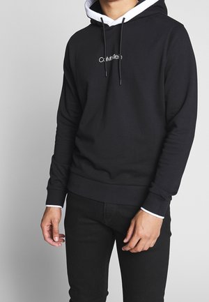 Sudadera negra con cordones blancos y forro interior. Presenta un pequeño logotipo blanco en el pecho, puños y dobladillo acanalados.