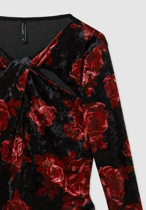 Top in velluto nero con maniche lunghe, caratterizzato da motivi di rose rosse, un dettaglio frontale attorcigliato e una leggera lucentezza. Etichetta del marchio: Calliope.