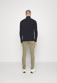 Svart ribbad polotröja med figurnära design. Olivgröna byxor med smal passform. Vita sneakers med svarta detaljer, minimalistisk stil.