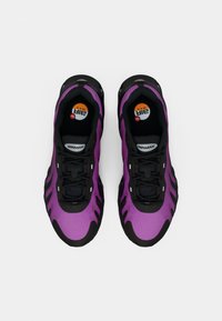 Par u crnih i ljubičastih Nike Air Max tenisica viđenih odozgo na bijeloj pozadini.