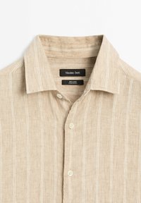 Linen shirt in light beige with white vertical stripes, featuring a pointed collar and button closures. Labels visible inside collar.