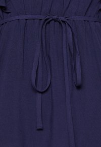 Námořnická látka s texturovaným povrchem, s nařaseným pasem a vázáním na zavazování. Materiál vypadá měkce a je lehký.