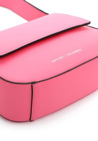 Bolso cruzado sintético rosa con cierre de solapa, ribete negro y detalles del logo plateado; textura suave y forma rectangular.