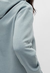 Felpa blu chiaro realizzata in morbido cotone misto, con vestibilità comoda e cappuccio spazioso. Presenta dettagli di cucitura discreti sulle spalle.