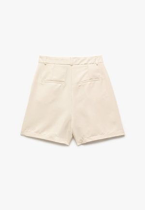Pantalones cortos crema con una textura suave, con cintura alta, bolsillos traseros y un acabado ajustado. Bordes dobladillados con un detalle de costura mínima.