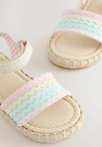 Sandales pour enfants beige avec semelles tissées et brides à motifs ondulés pastel rose, bleu et vert.