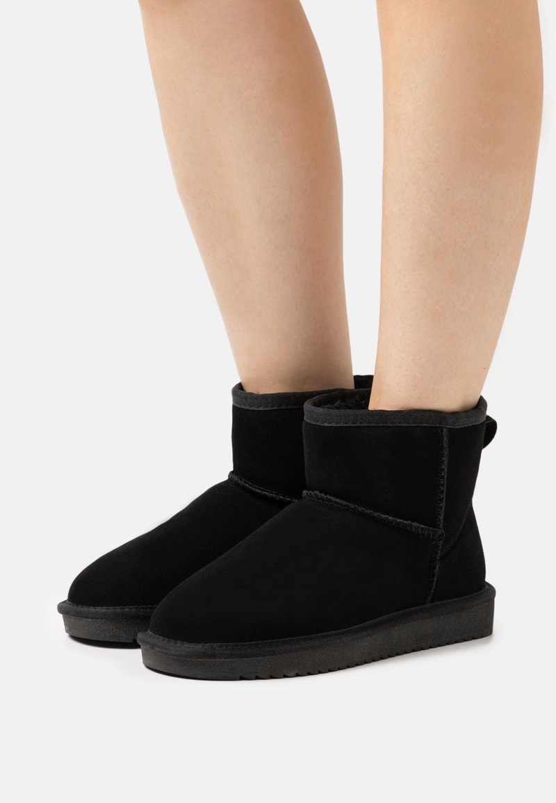 Bottines en suède noir avec un bout arrondi, doublure douce et coutures le long des seams. Semelle en caoutchouc basse avec une adhérence texturée.
