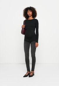 Čierne tričko s dlhým rukávom a skráteným strihom, skombinované s tmavosivými úzkymi džínami a čiernymi opätkami, spolu s vínovo červenou crossbody kabelkou.