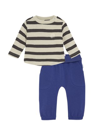 Gestreiftes Langarmshirt in Creme und Dunkelgrau, kombiniert mit blauen elastischen Hosen mit Taschen vorne und umgeschlagenen Knöcheln.
