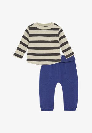 Gestreiftes Langarmshirt in Creme und Dunkelgrau, kombiniert mit blauen elastischen Hosen mit Taschen vorne und umgeschlagenen Knöcheln.