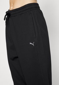 Pantalones de chándal negros hechos de una tela suave, con una cinturilla elástica y cordón ajustable, además de un pequeño logo de Puma gris en el costado.