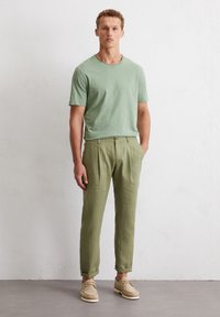 Mint green short-sleeve t-shirt, paired with light olive green linen trousers; beige suede shoes; casual fit with rolled cuffs on pants.