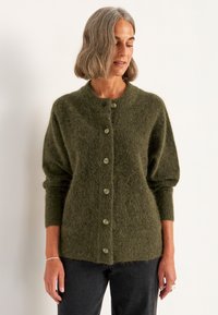 Grüne, flauschige Strickjacke mit rundem Ausschnitt, Knopfverschluss, langen Puffärmeln und strukturiertem Oberflächenmaterial. Eignet sich gut für schichtweise Outfits.