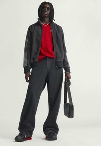 Črna bomberska jakna s črtastimi rokavi, rdeča majica, in ohlapne črne kavbojke. Črne superge z rdečimi detajli in mala črna torbica čez rame.