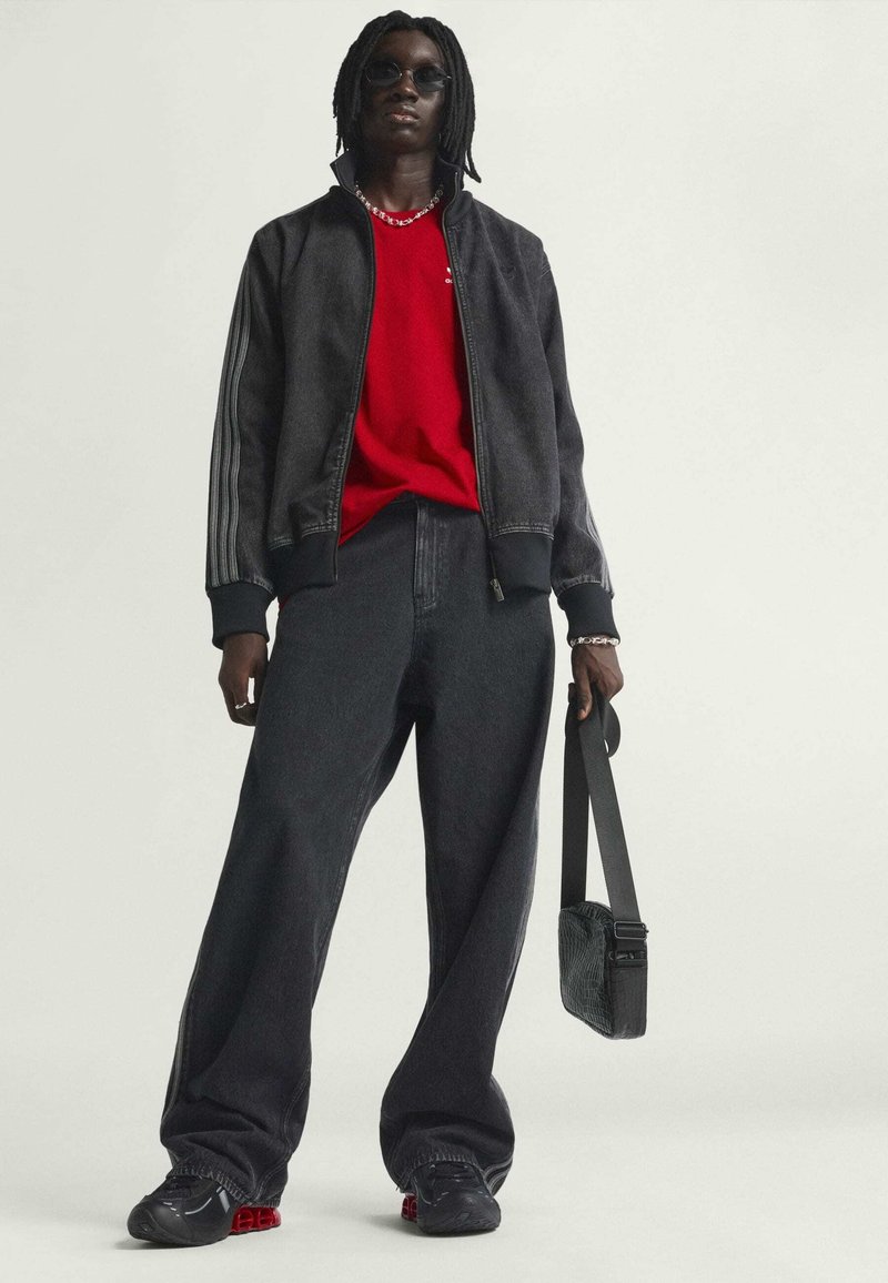 Črna bomberska jakna s črtastimi rokavi, rdeča majica, in ohlapne črne kavbojke. Črne superge z rdečimi detajli in mala črna torbica čez rame.