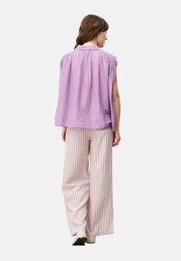 Lavendelfarbenes ärmelloses Oberteil mit gerafftem Ausschnitt, kombiniert mit weit geschnittenen gestreiften Hosen in Weiß, Orange und Blau. Glatter Stoff, lockere Passform.