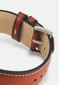 Brauner Lederarmband mit glatter Oberfläche, kontrastierenden weißen Nähten und einer silbernen Metallschließe mit Keeper-Schlaufen.
