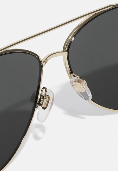 Occhiali da sole dorati con lenti scure, forma rotonda, montatura in metallo, con dettagli sui cuscinetti nasali e sottili accenti in metallo.