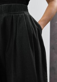 Pantaloni negri plisati cu o textură netedă, având buzunare laterale și o talie înaltă gătită, într-un design casual.