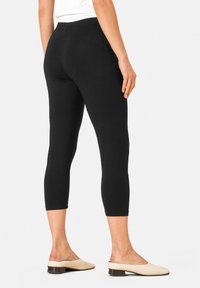 Zwart enkel-lange leggings met een gladde textuur en een aansluitend ontwerp, gecombineerd met lichtcrème instappers met een lage hak.