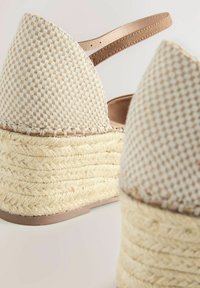 Szőtt bézs espadrille wedge szandál texturált felsőrésszel, bokapánttal és jutával bevont sarokkal. Lapos, széles talpa stabilizálja a kivitelezést.