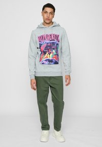 Grå hettegenser med et fargerikt grafisk trykk med ordet "WONDERFUL," kombinert med grønne bukser og hvite sneakers.