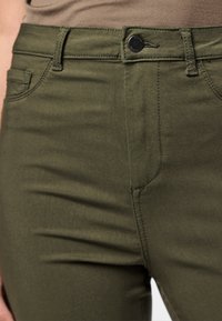 Olive green pants made of stretch fabric, featuring a button closure, front pockets, and subtle stitching details along the seams.