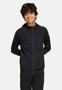 Schwarze Zip-Hoodie aus weichem Material, mit einer Kängurutasche, strukturierten Ärmeln und einem adidas-Logo auf der linken Brust.