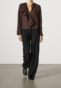 Ruske pleated wrap bluză cu decolteu în V adânc și mâneci lungi, combinată cu pantaloni negri largi și cizme negre până la gleznă. Design minimalist.