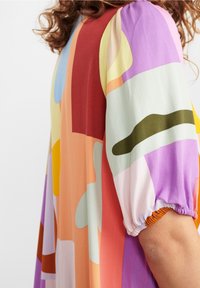Robe à motifs colorés avec manches bouffantes, confectionnée en tissu lisse aux formes abstraites dans des tons orange, violet, vert et bleu.