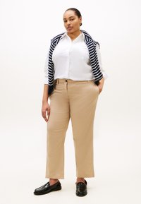 Μπεζ παντελόνια με ίσια γραμμή συνδυασμένα με λευκό πουκάμισο με κουμπιά. Μια μπλε ναυτικού και λευκή ριγωτή ζακέτα καλύπτει τους ώμους. Μαύρα μοκασίνια ολοκληρώνουν το σύνολο.