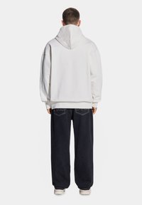 Biała bawełniana bluza z kapturem ze sznurkiem, w połączeniu z ciemnoniebieskimi spodniami typu wide-leg z tylnymi kieszeniami i jasnym przeszyciem.