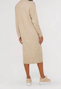 Robe-pull tricotée beige avec ourlet et poignets côtelés, présentant une coupe décontractée et une longueur mi-mollet, associée à des baskets beige clair.