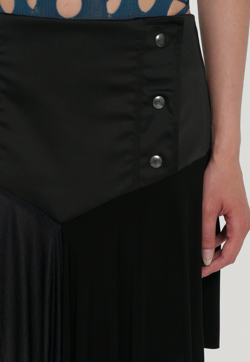 Black skirt featuring satin and pleated textures, with a diagonal design and three metal buttons on the waistband.
