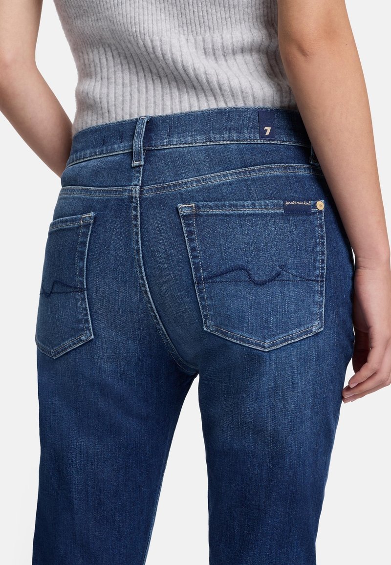Ciemnoniebieskie dżinsy o slim fit, z średnim stanem, dwiema tylnymi kieszeniami i subtelnymi detalami stichingu na krawędziach kieszeni.