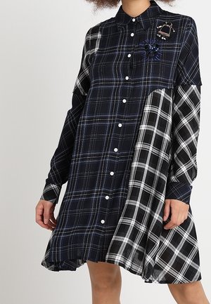 Sukienka z długim rękawem zapinana na guziki, z mieszanymi wzorami w kratę w kolorach czarnym, białym i granatowym, zdobiona ozdobnymi broszkami na piersi.