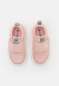 Jasnoróżowe buty sportowe z siateczką i materiałem syntetycznym, wyposażone w pasek na rzep, małą szarą zakładkę oraz subtelny detal z logo.