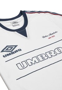 Hvid sports skjorte med marineblå krave og detaljer. Har stort marineblått "UMBRO" logo samt mindre broderet "Umbro Manchester siden 1924."