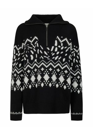 Femme debout portant un pull à motif noir et blanc, des leggings noirs et des bottes d'hiver noires sur fond blanc.