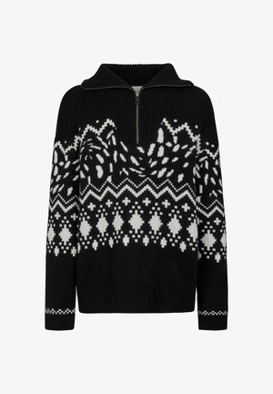 Femme debout portant un pull à motif noir et blanc, des leggings noirs et des bottes d'hiver noires sur fond blanc.