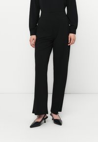 Zwarte high-waisted broek met een rechte pijpontwerp, een gladde textuur en geen zichtbare naden, gecombineerd met puntige zwarte hakken.