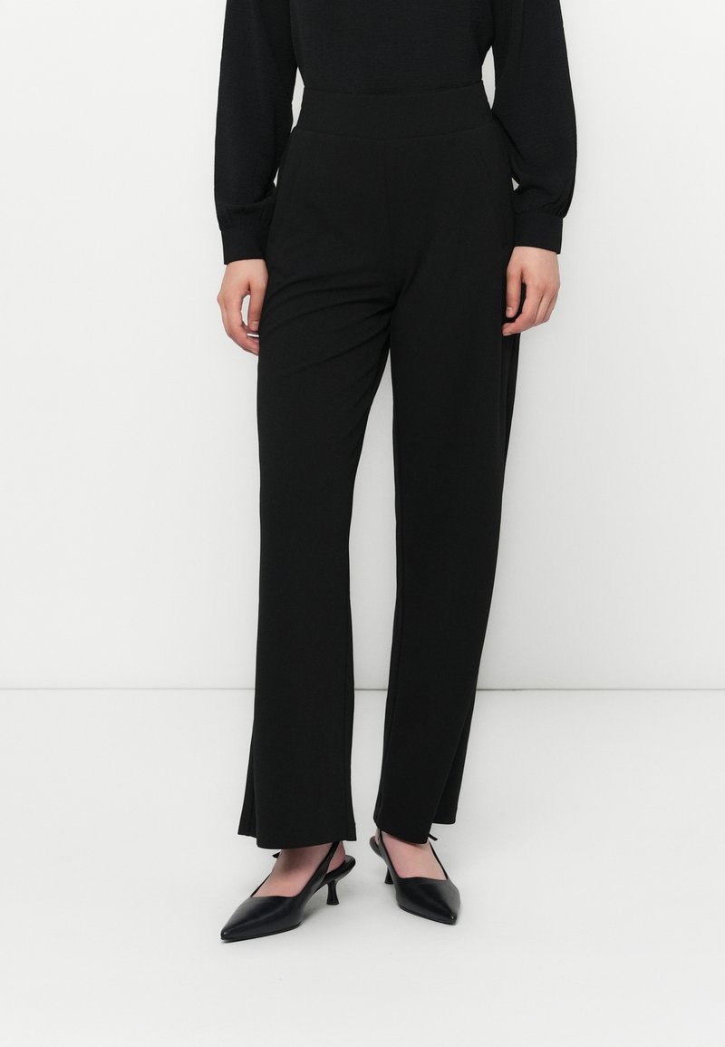 Zwarte high-waisted broek met een rechte pijpontwerp, een gladde textuur en geen zichtbare naden, gecombineerd met puntige zwarte hakken.