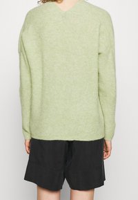 Ljusgrön, stickad tröja med lös passform och V-ringning; texturerat tyg och långa ärmar. Kombineras med svarta, välsydda shorts.