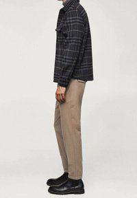 Veste à carreaux noirs et gris, coupe décontractée, accompagnée d'un pantalon beige clair fuselé et de bottines en cuir noir. Tissu soigné et texturé.