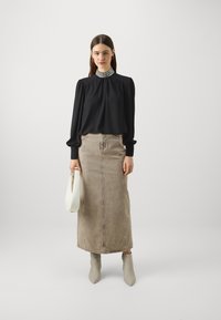 Blusa nera con scollatura arricciata e colletto di perline, gonna di jeans beige e stivali alla caviglia grigi chiari. La modella tiene una borsa bianca.