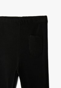 Musta ribbatus leggings, jossa on joustava vyötärö ja pieni tasku sivussa. Materiaali on pehmeä ja venyvä.